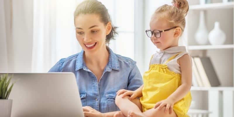 Woman working on laptop with child sitting beside her