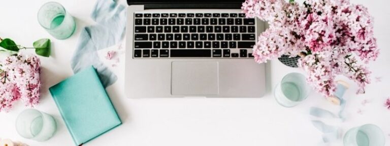 open laptop surrounded by pink flowers and green notebook