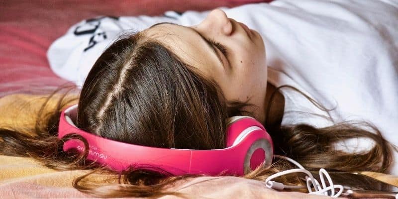 teenage girl laying down listening to music via pink headphones 